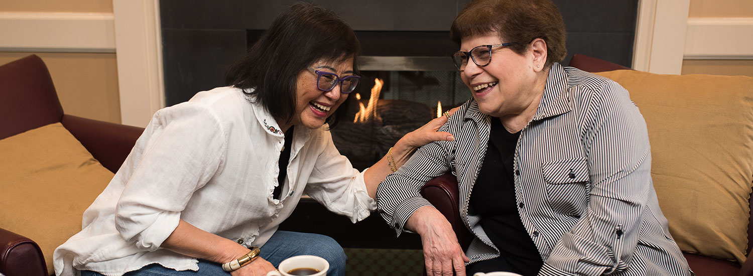 Women smiling and laughing over cups of coffee